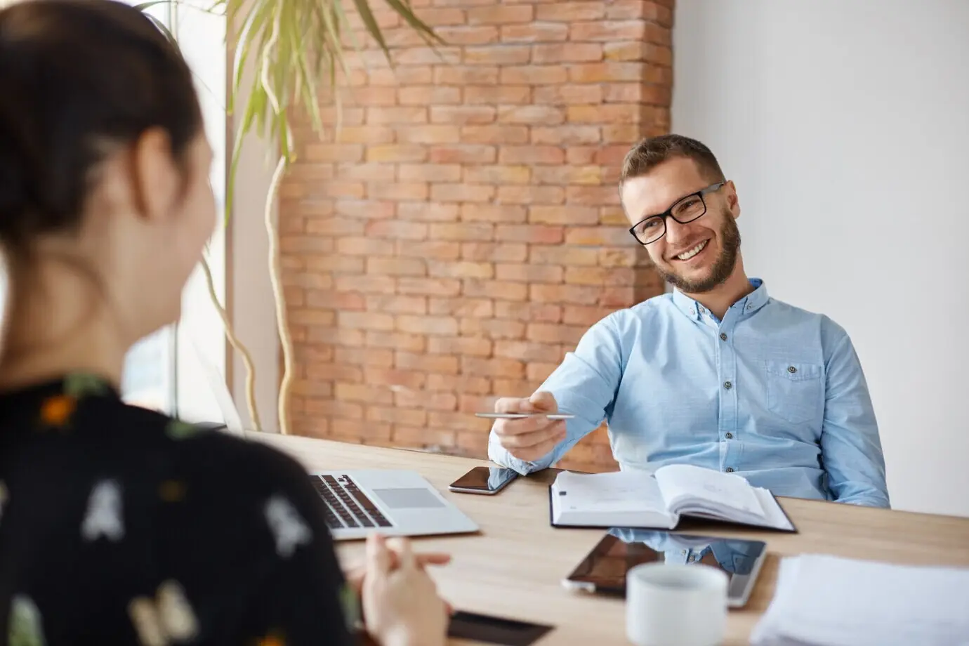 Бизнес-концепция. Молодая темноволосая женщина на собеседовании сидит напротив зрелого жизнерадостного офисного менеджера, они непринуждённо беседуют о её опыте и степени образования.